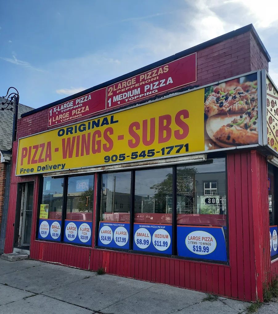 Original Pizza’s familiar red storefront and yellow Pizza, Wings, Subs sign on Main Street East